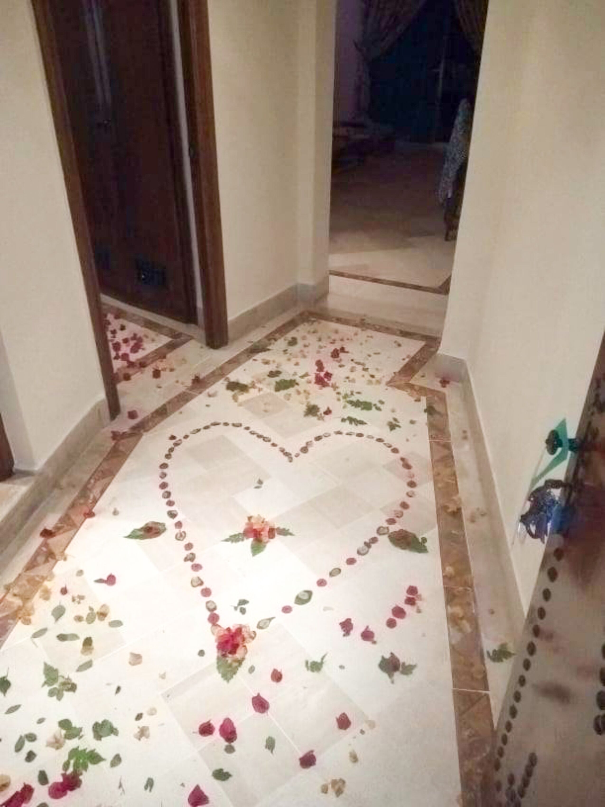 Un pasillo con piso de baldosas que presenta un diseño en forma de corazón y pétalos de rosa esparcidos.