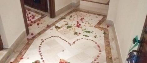 Un pasillo con piso de baldosas que presenta un diseño en forma de corazón y pétalos de rosa esparcidos.