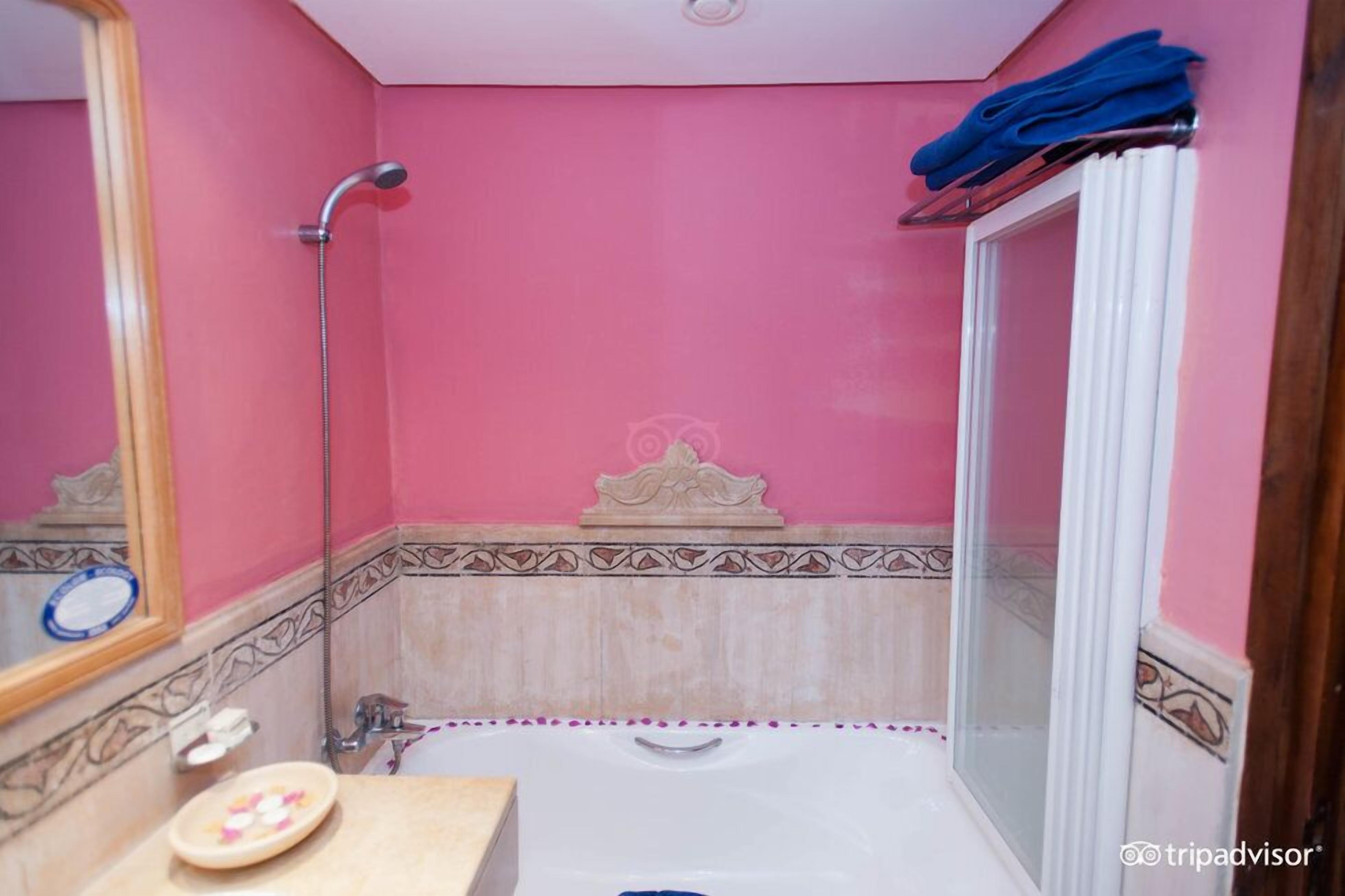 Un baño con pared rosa, una bañera, ducha y tocador con espejo.