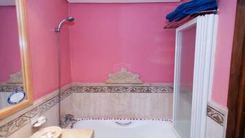 Un baño con pared rosa, una bañera, ducha y tocador con espejo.