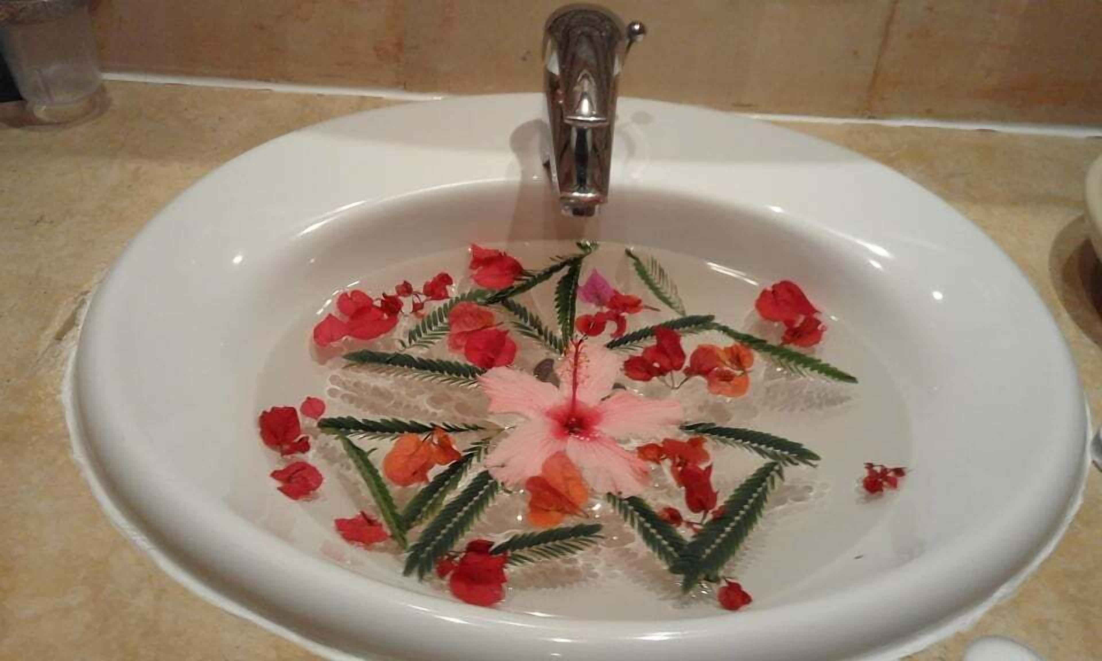 A bathroom sink with water, red flowers, and green leaves.