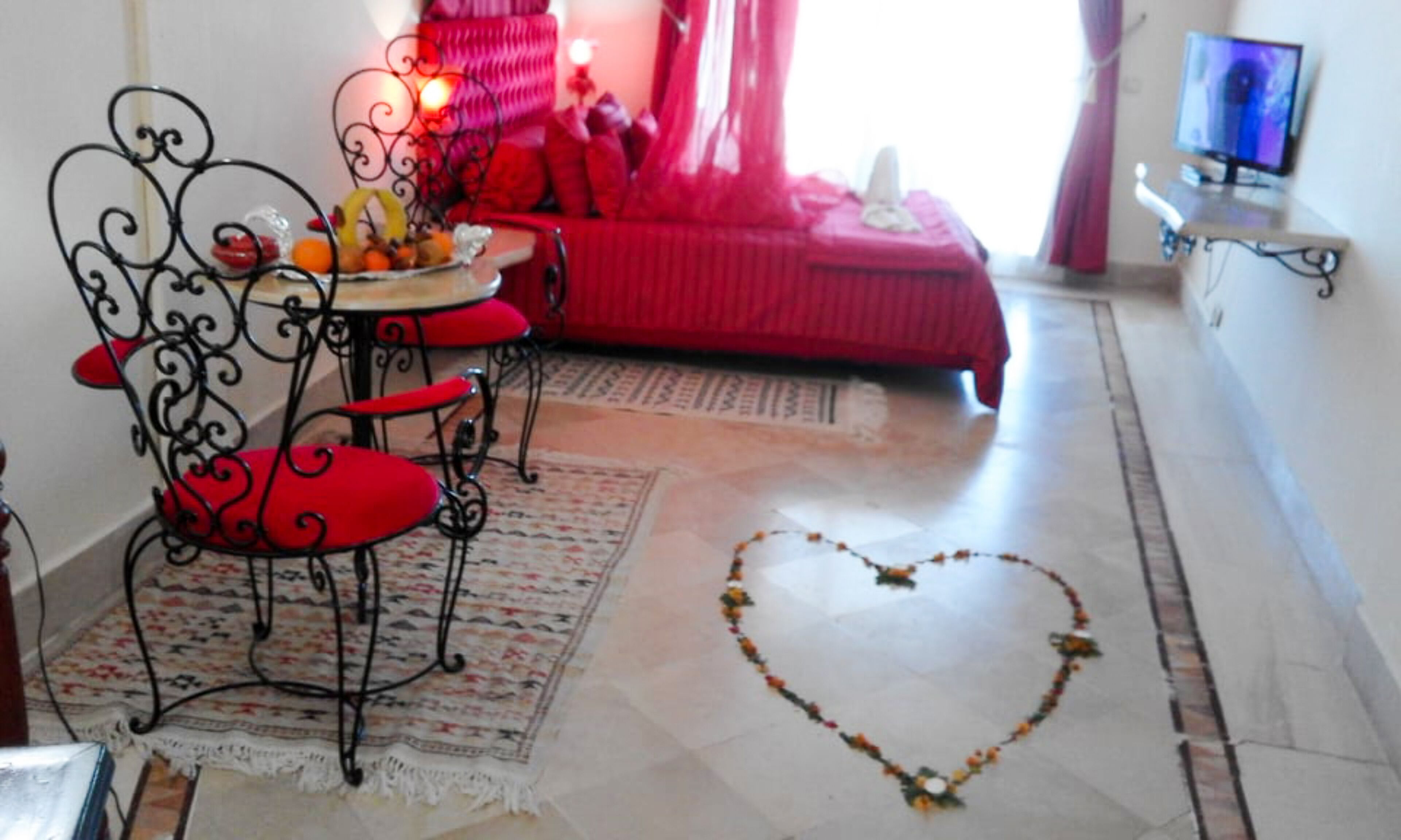 A living room with a red sofa, a coffee table with fruit, and a heart-shaped decoration on the floor.