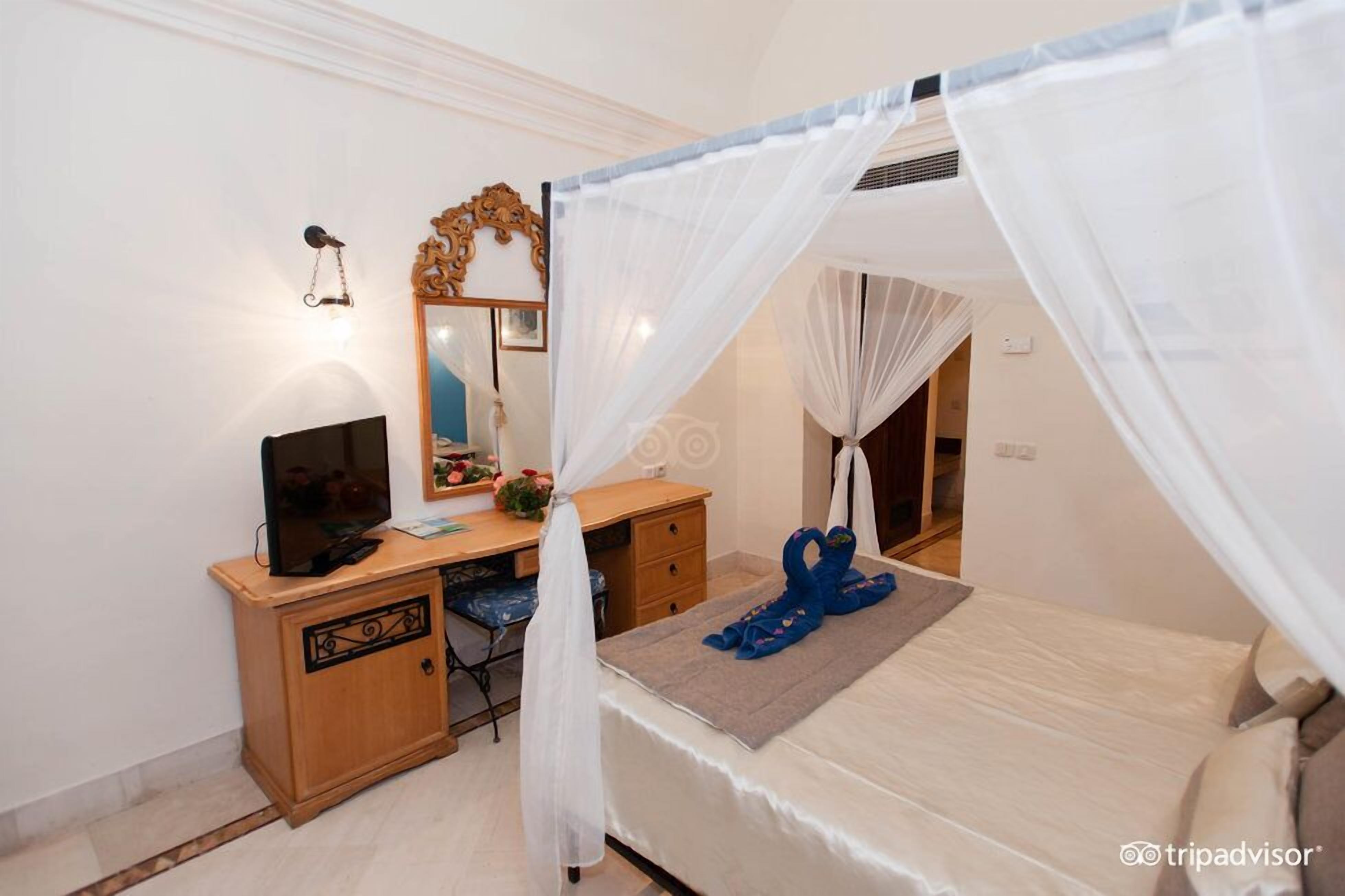 A bedroom with a bed, a desk, a chair, a television, and a mirror.