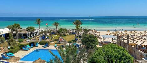 Un resort con piscina, zona de playa y palmeras.