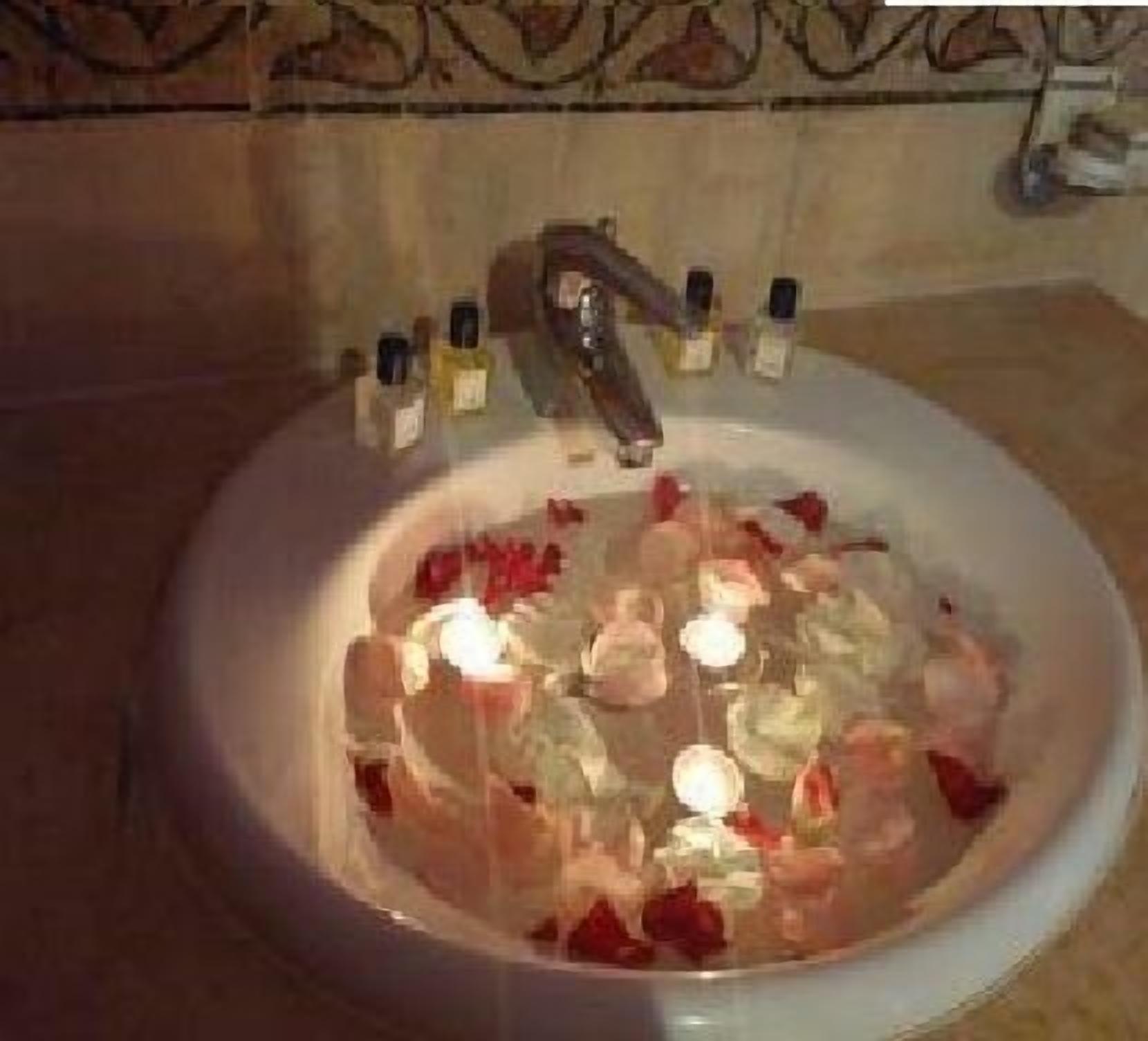 A bathroom sink with rose petals and candles.