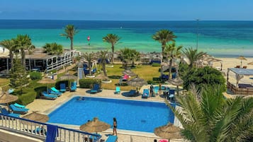 Relax by the pool or on the adjacent beach, surrounded by palm trees and lounge chairs.