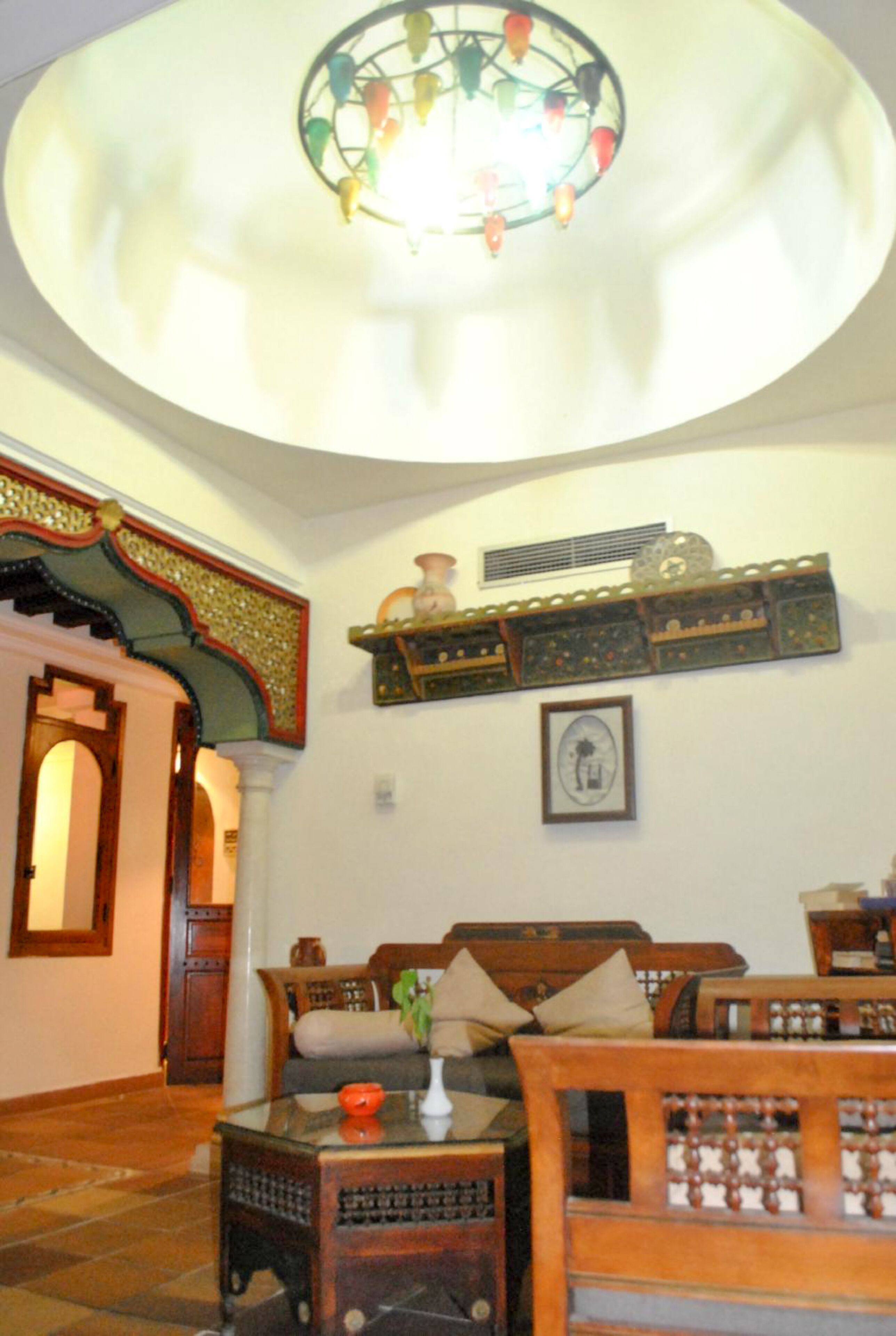 A traditional room with a wooden sofa, a glass coffee table, and a decorative ceiling light.