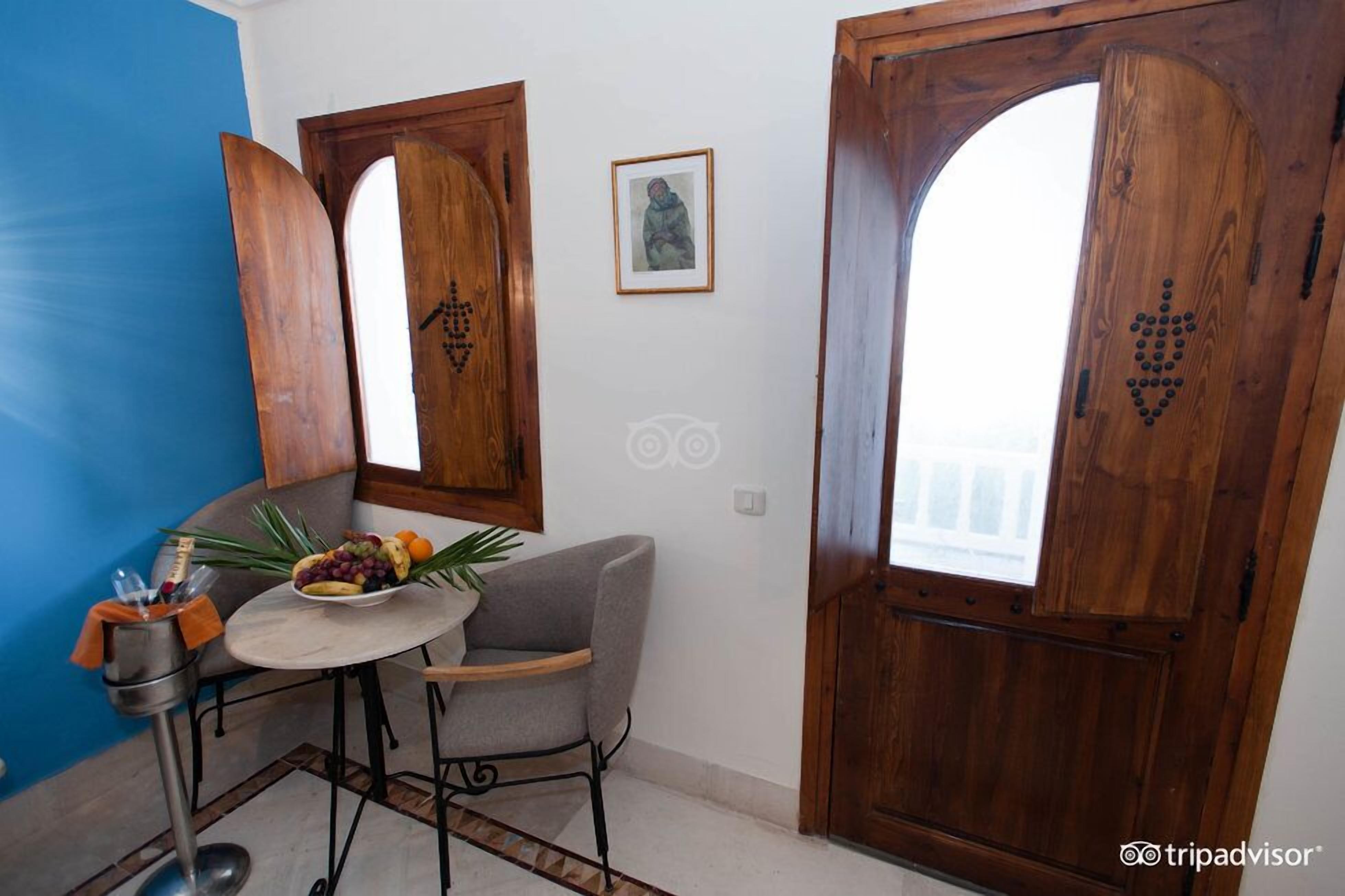 Una habitación con una puerta de madera, un cuadro en la pared y una mesa con frutas y un florero.