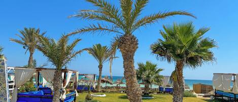A beachside resort with palm trees, blue lounge chairs, and thatched-roof huts.