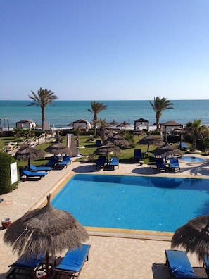A pool area with lounge chairs and umbrellas, a clear view of the ocean, and a tropical setting. - Hotel Dar el Bhar (Mezraia)