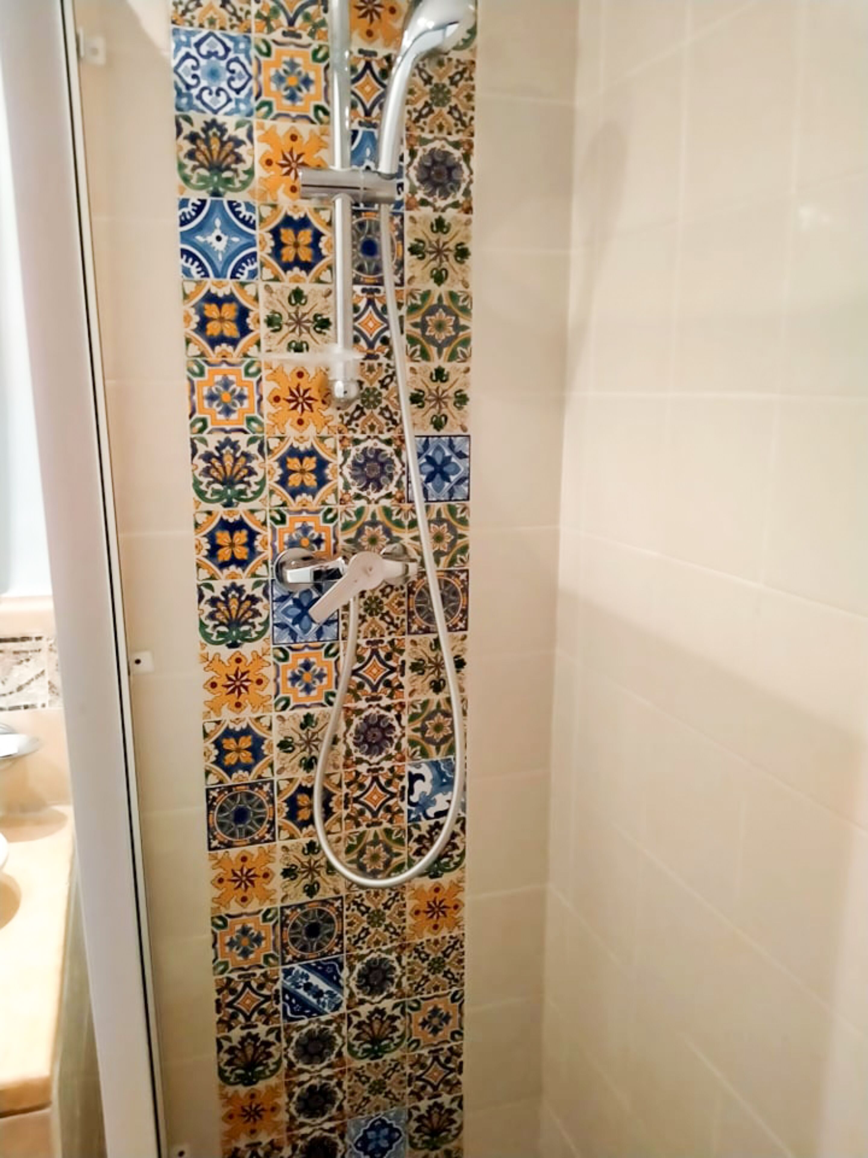 Ducha con salpicadero de azulejos coloridos y cabezal de ducha de mano.