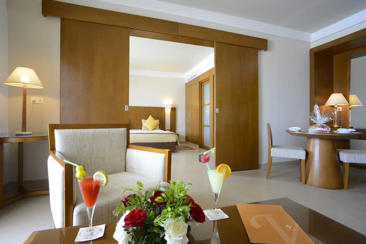 A hotel room with a bed, a sitting area with a table, and a dining area with a table and chairs.
