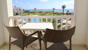 A balcony with wicker chairs and a white table, overlooking a beach and a pool. - Vincci Helios Beach (Aghir)