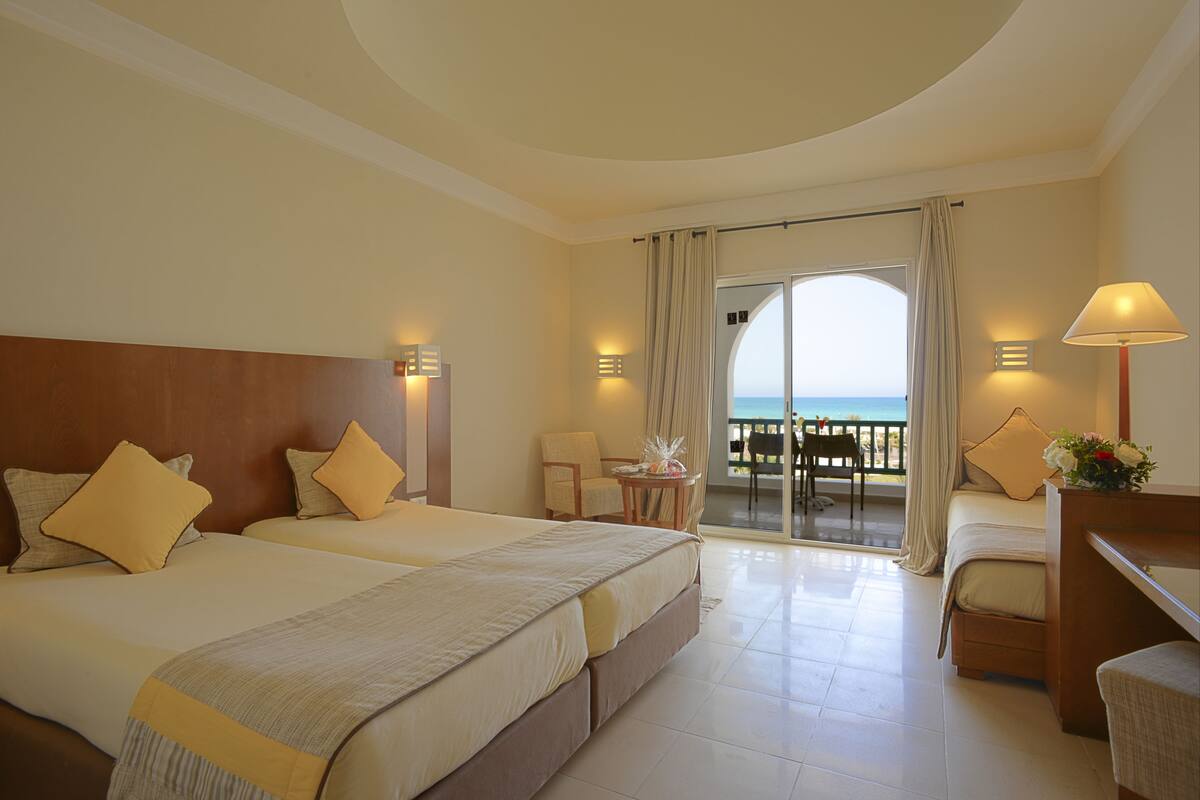 A hotel room with two beds, a balcony, and a view of the sea.