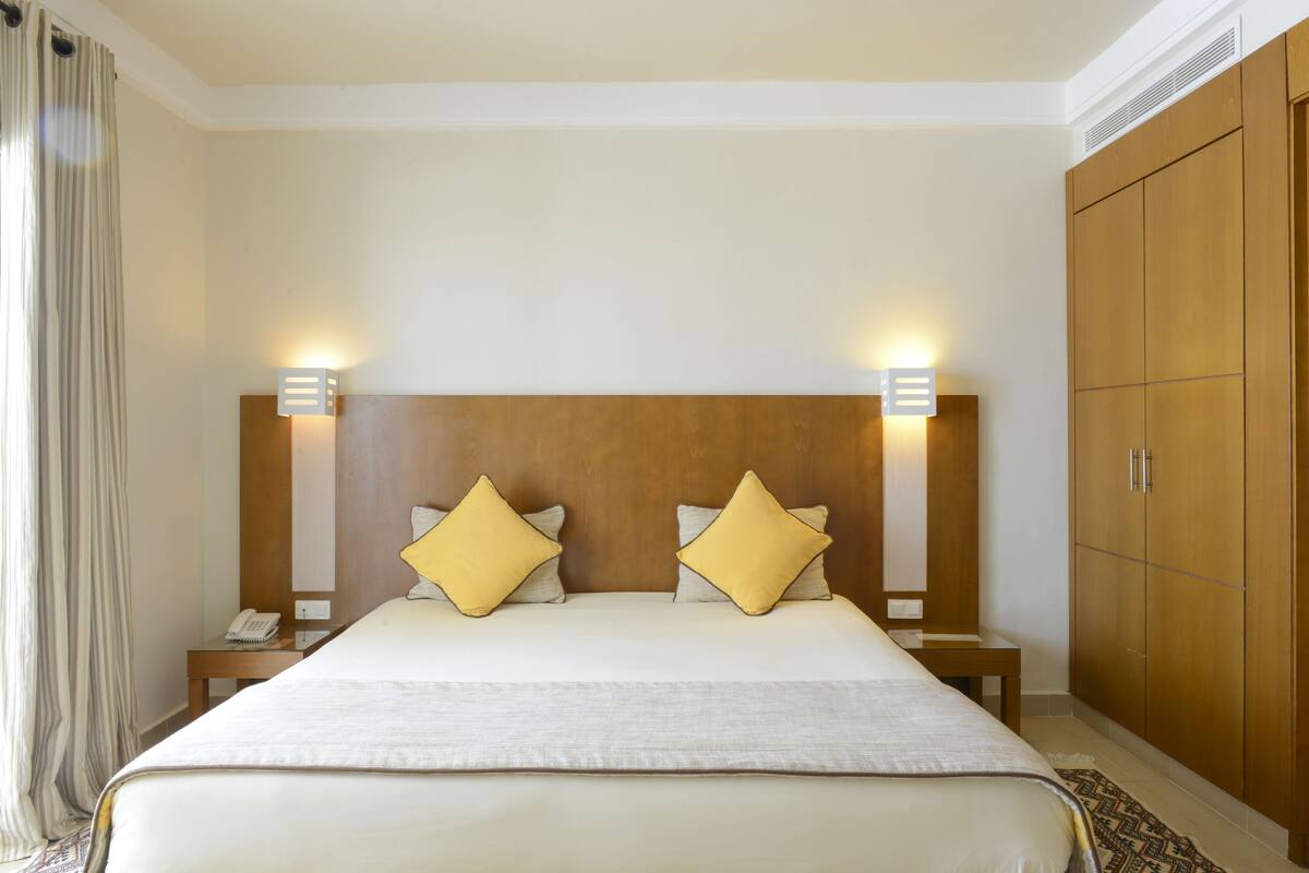 A hotel room with a large bed, two bedside lamps, a wooden wardrobe, and a telephone on the nightstand.