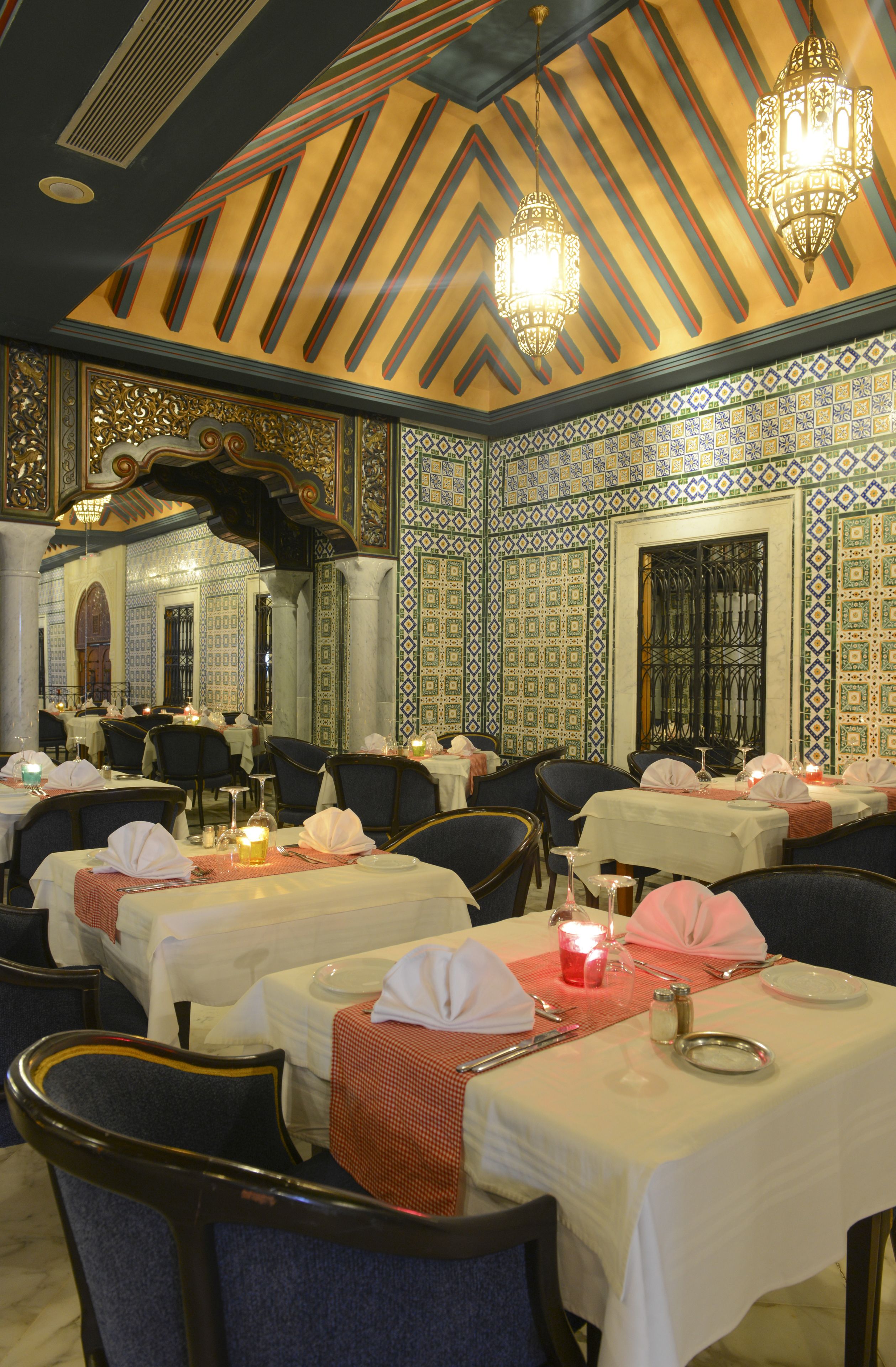 Un restaurante con mesas dispuestas para comer, con decoraciones ornamentales en el techo y las paredes, y candelabros.