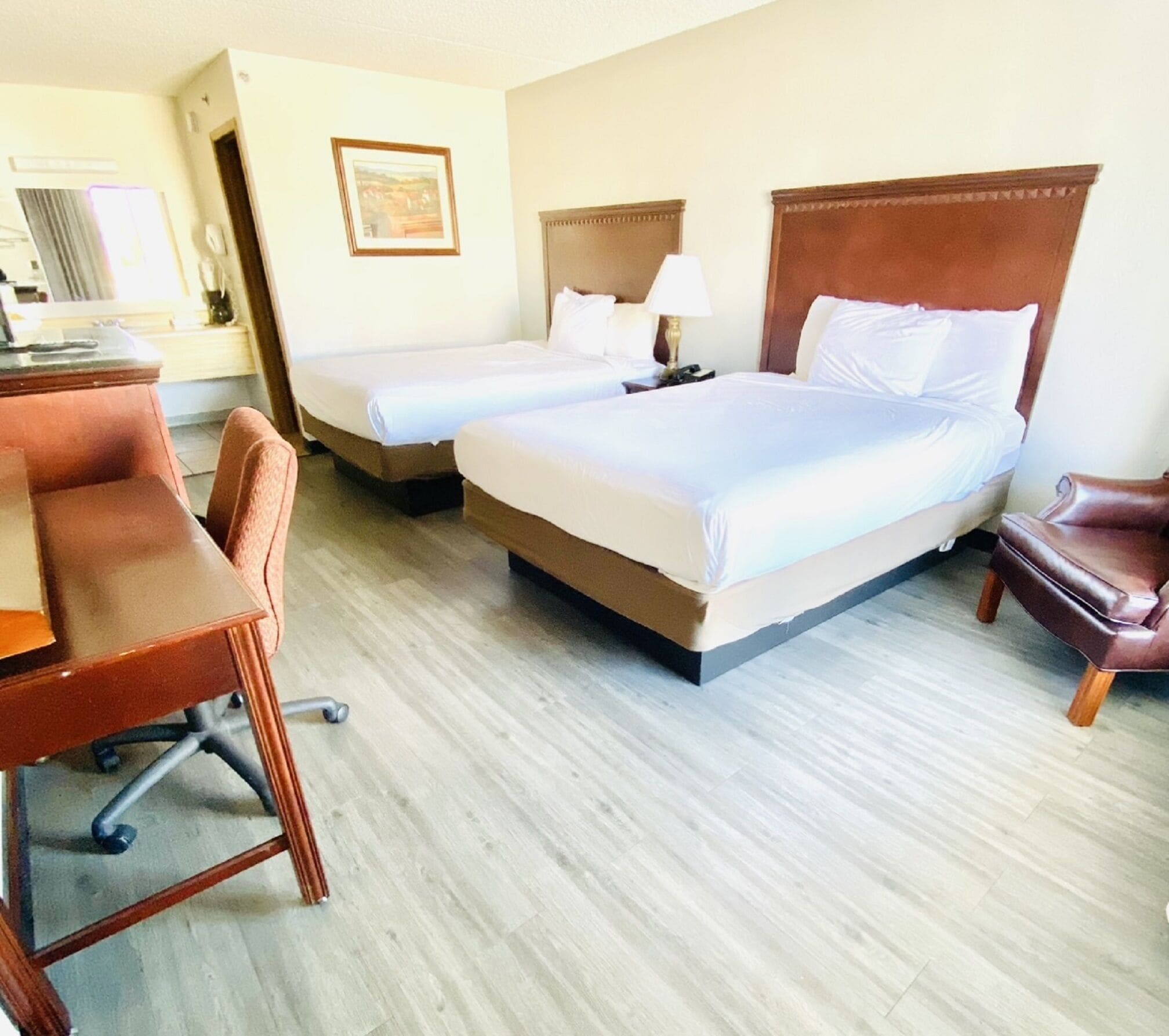 Une chambre d’hôtel avec deux lits, un bureau, une chaise et une lampe.