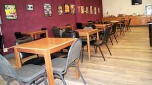 A dining area with multiple tables and chairs, a television mounted on the wall, and a kitchen area in the background. - Willow Tree Inn (Branson)