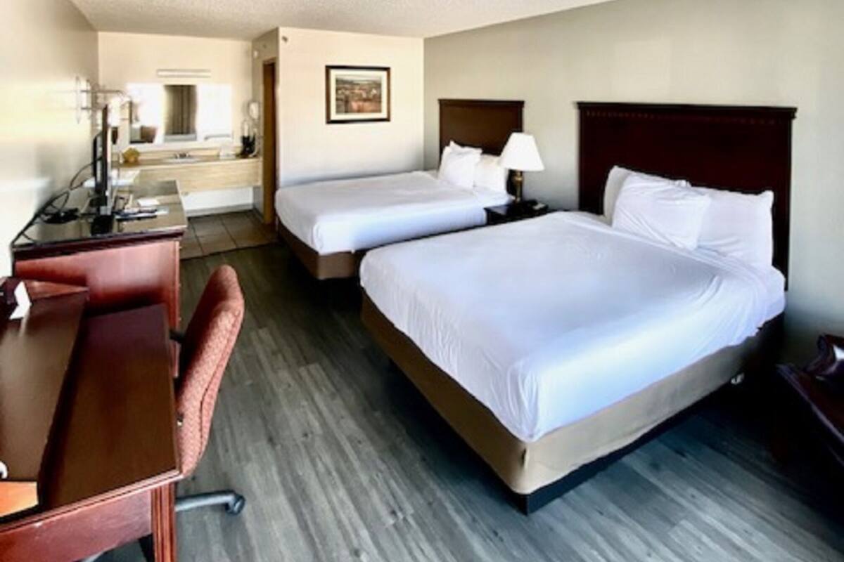 A hotel room with two beds, a desk, and a chair.