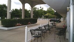 An outdoor patio area with tables and chairs, a white picket fence, and a covered walkway. - Willow Tree Inn (Branson)