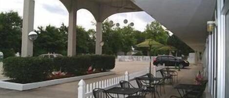 An outdoor patio area with tables and chairs, a white picket fence, and a covered walkway.