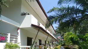A two-story building with a white facade, a covered porch with railings, and a pathway lined with greenery and flowers. - Patong Palace Hotel (Patong)