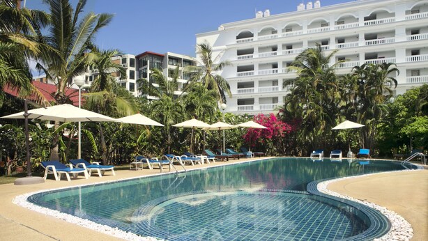 A swimming pool with blue tiles, surrounded by lounge chairs and umbrellas, with a hotel building in the background. - Patong Palace Hotel (Patong)