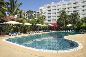 A swimming pool with blue tiles, surrounded by lounge chairs and umbrellas, with a hotel building in the background. - Patong Palace Hotel (Patong)