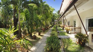 A pathway lined with potted plants and palm trees leading to a building with a tiled roof and a window with a towel hanging on a rack. - Patong Palace Hotel (Patong)