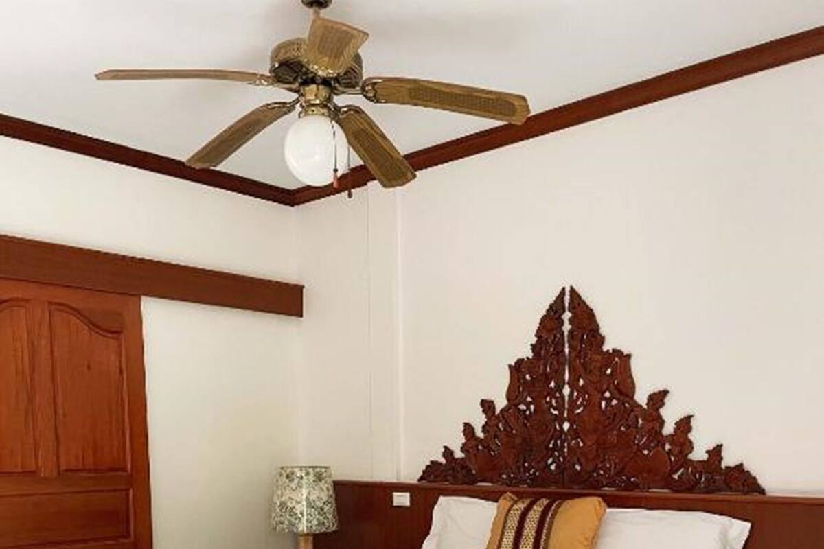 A wooden bed with a decorative headboard, a ceiling fan, and a nightstand with a lamp.