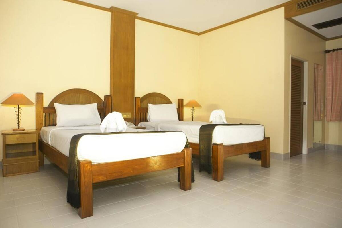 A hotel room with two wooden beds, each with a nightstand and a lamp.