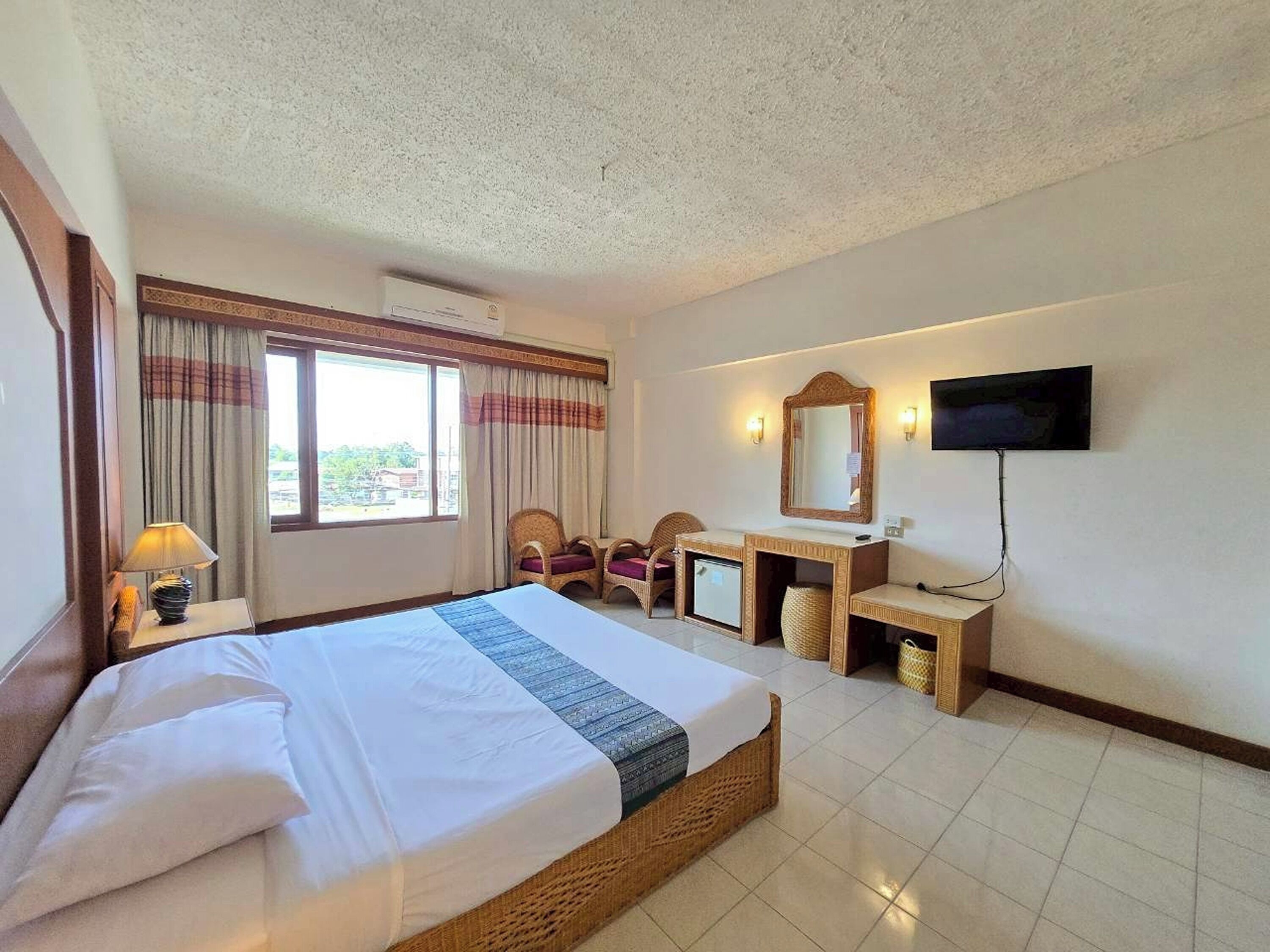 Ein Hotelzimmer mit einem großen Bett, einem Schreibtisch inklusive Spiegel, einem Fernseher und einem Fenster mit Vorhängen.