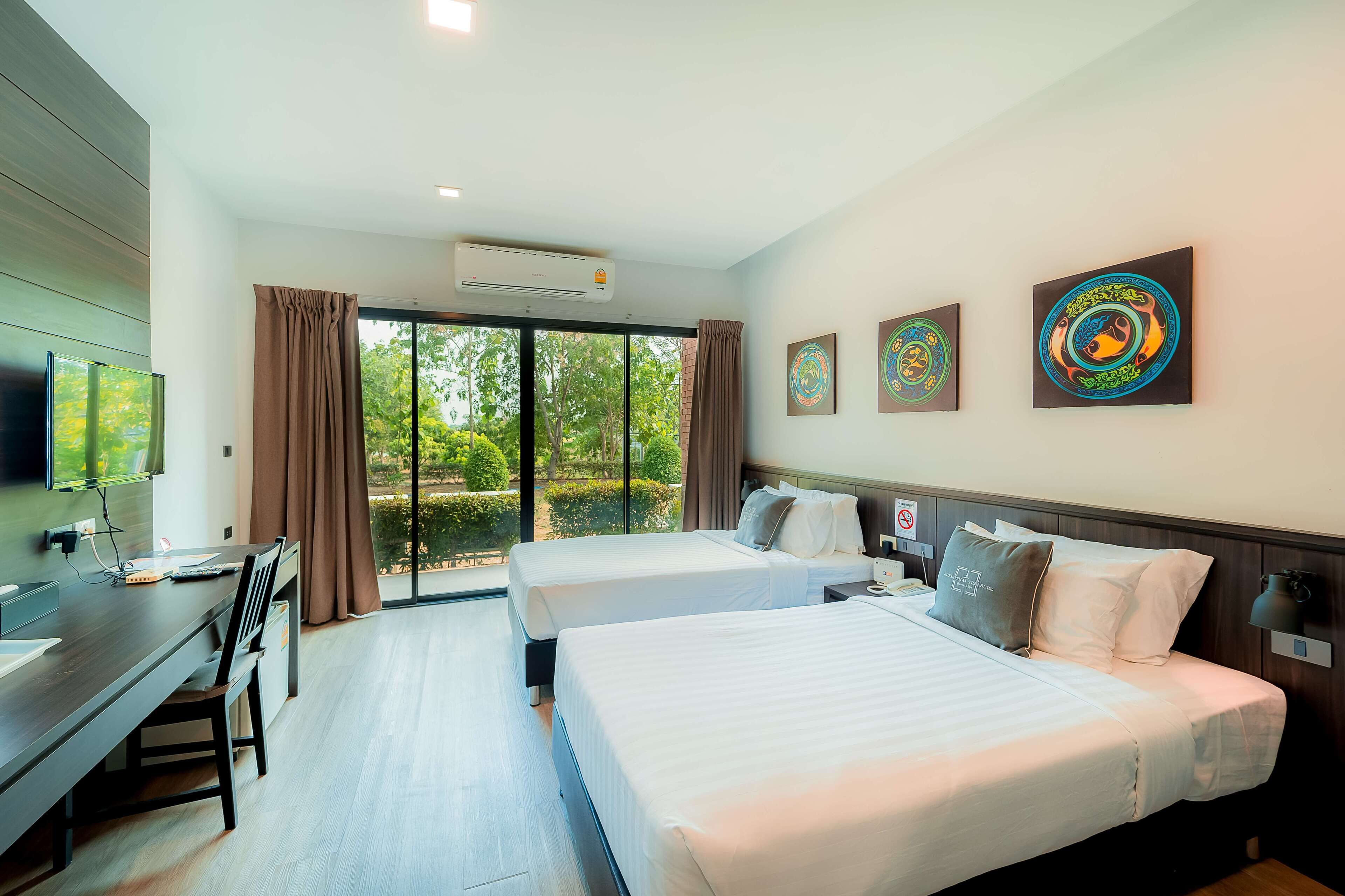 A hotel room with two beds, a desk, a TV, and artwork on the wall.