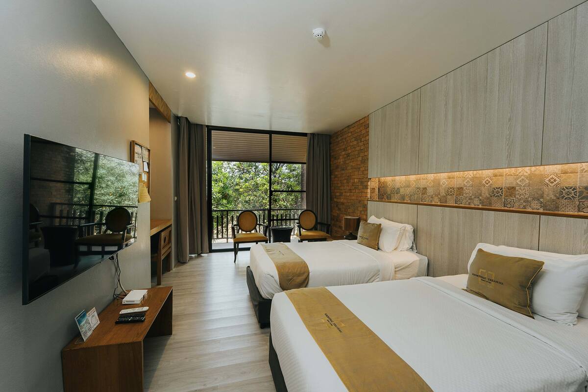 A hotel room with two beds, a TV, a desk, and a balcony with chairs.