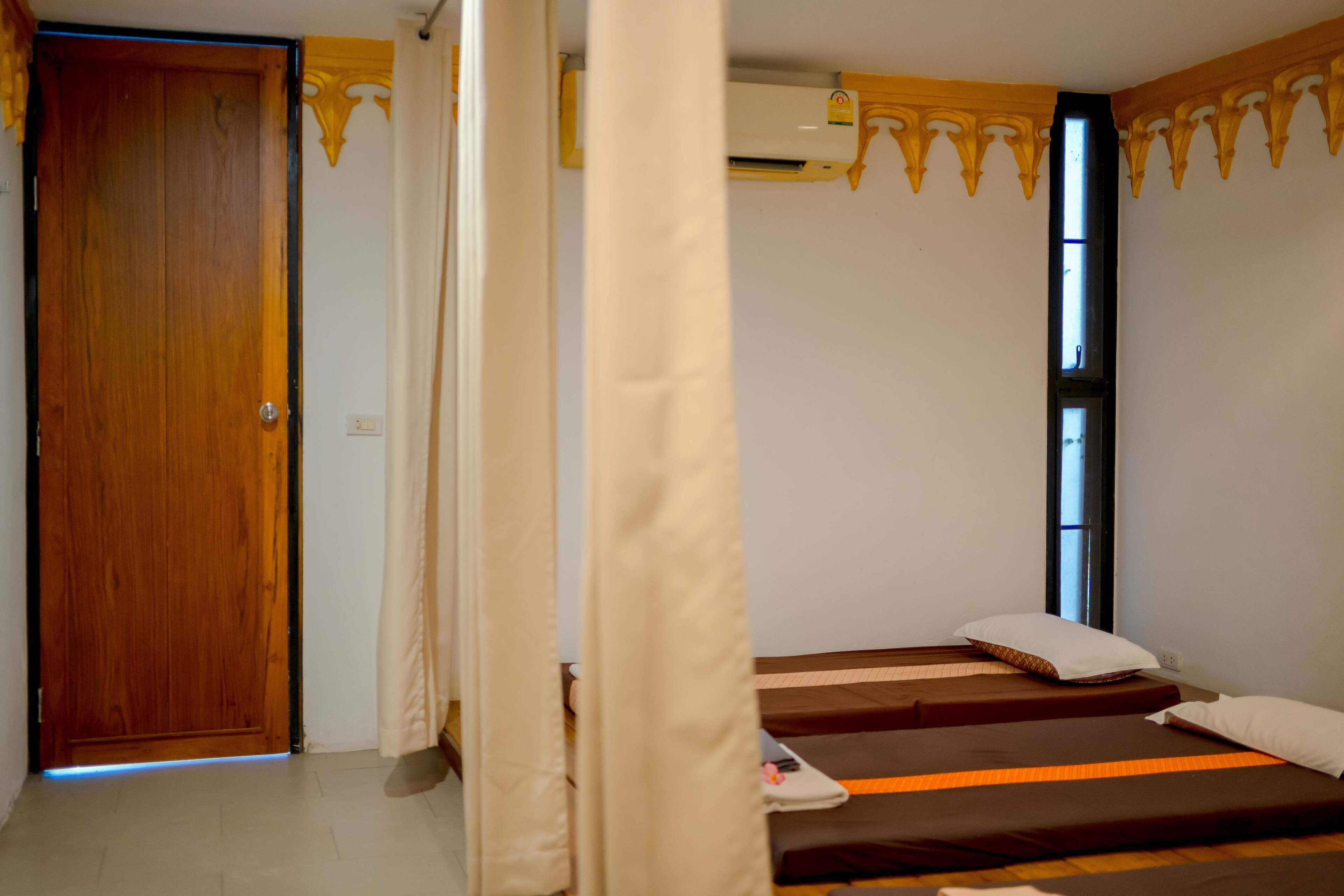Una habitación con una puerta de madera, una cama con colchón marrón y almohada blanca, y una ventana con cortinas.