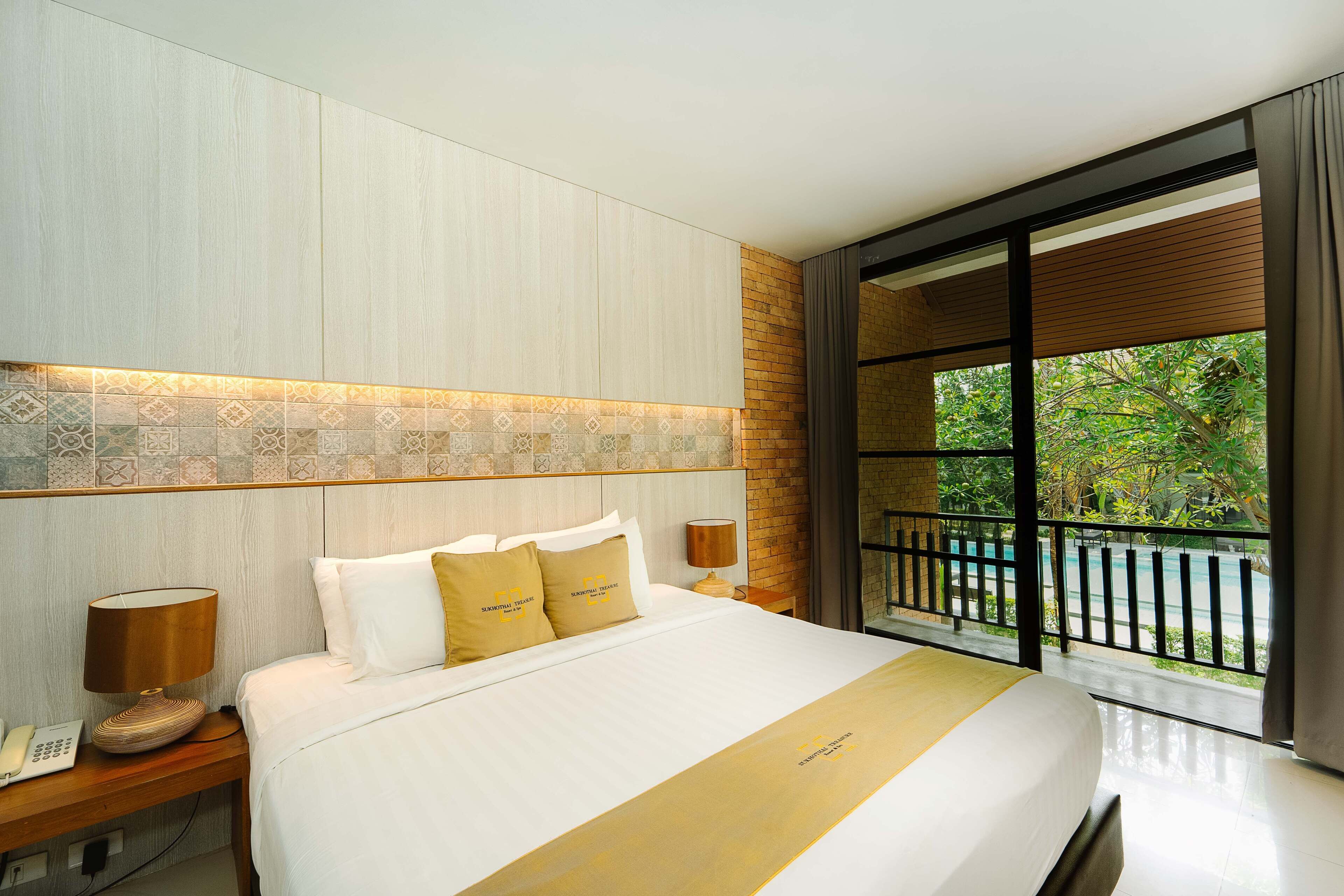Habitación de hotel con una cama grande, una mesita de noche con lámpara y vista a una piscina a través de un ventanal.