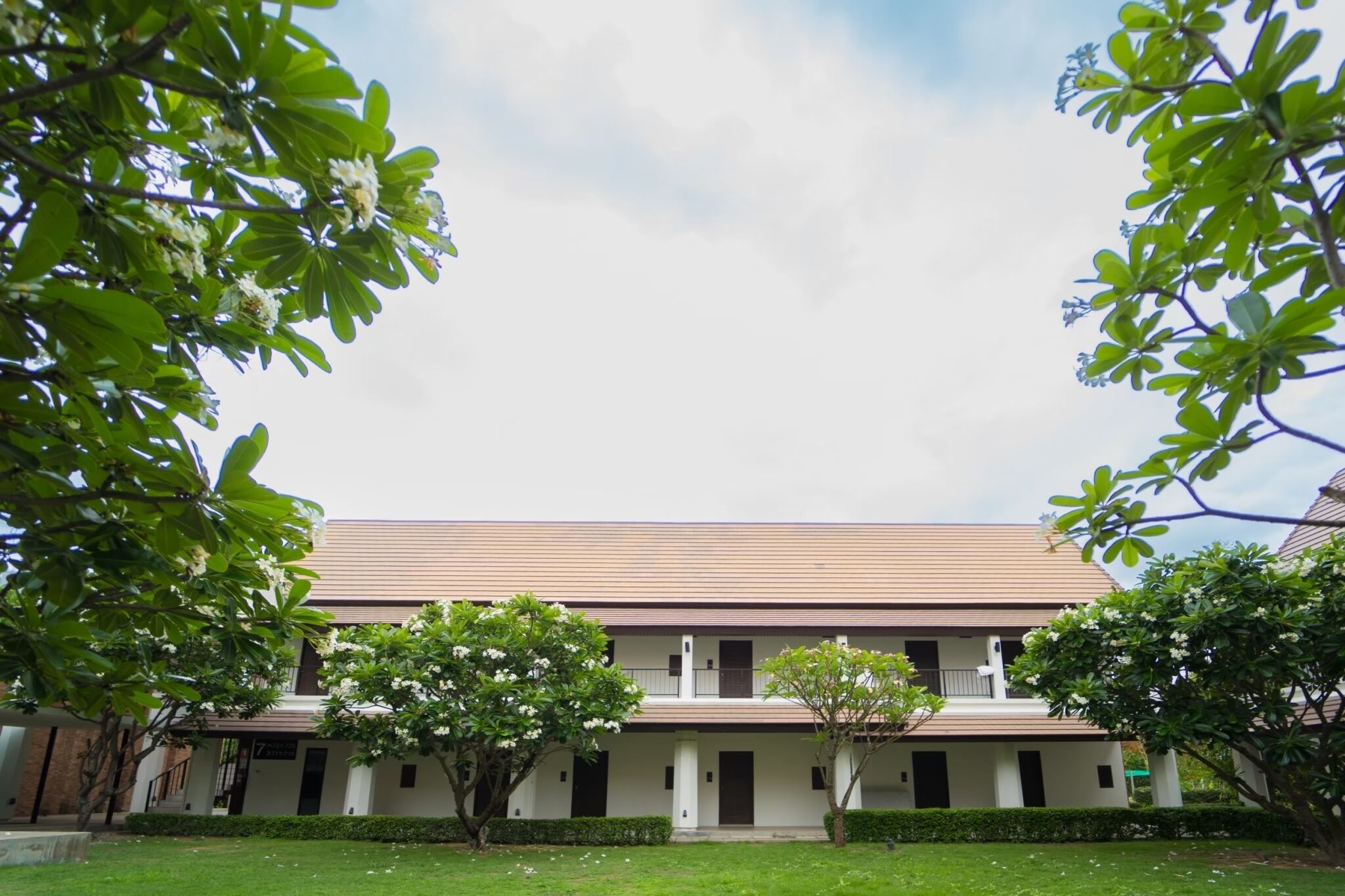 A two-story building with a flat roof, surrounded by greenery and trees.