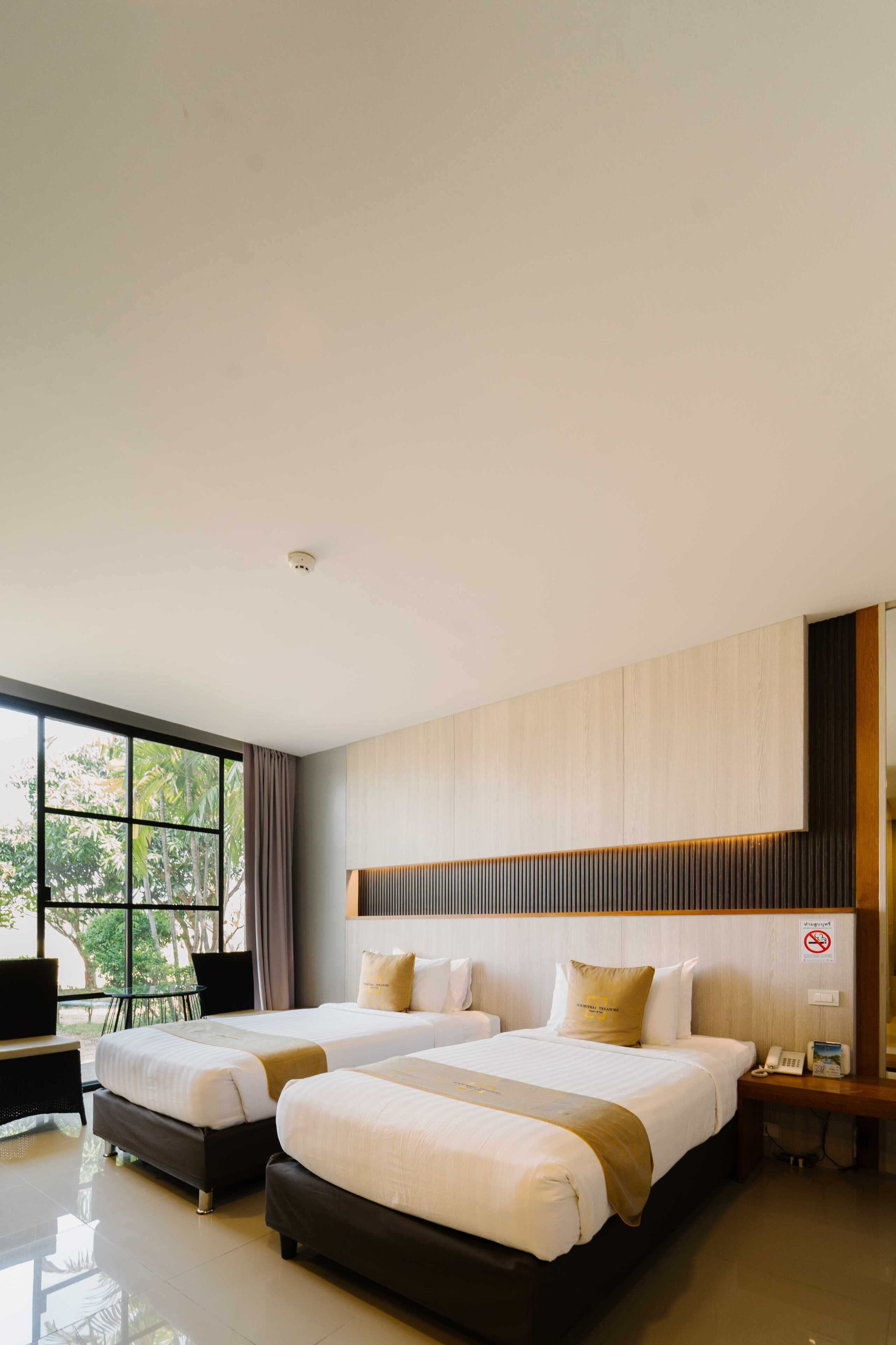 Habitación de hotel con dos camas, un ventanal grande y vistas al verde exterior.
