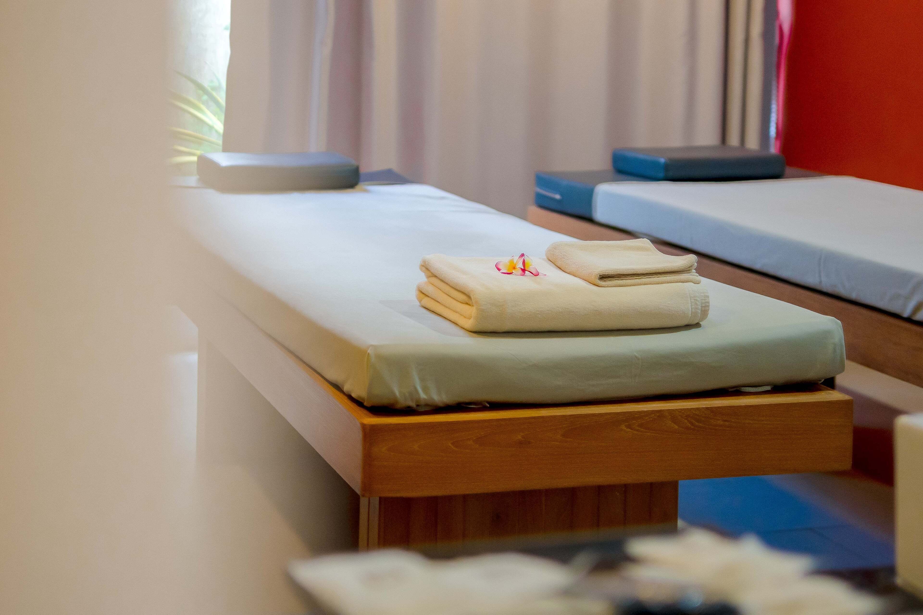 Un letto singolo con una testiera in legno, un asciugamano piegato con cura e un piccolo fiore sul letto.