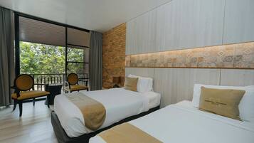 A hotel room with two beds, a balcony with chairs, and a view of greenery.