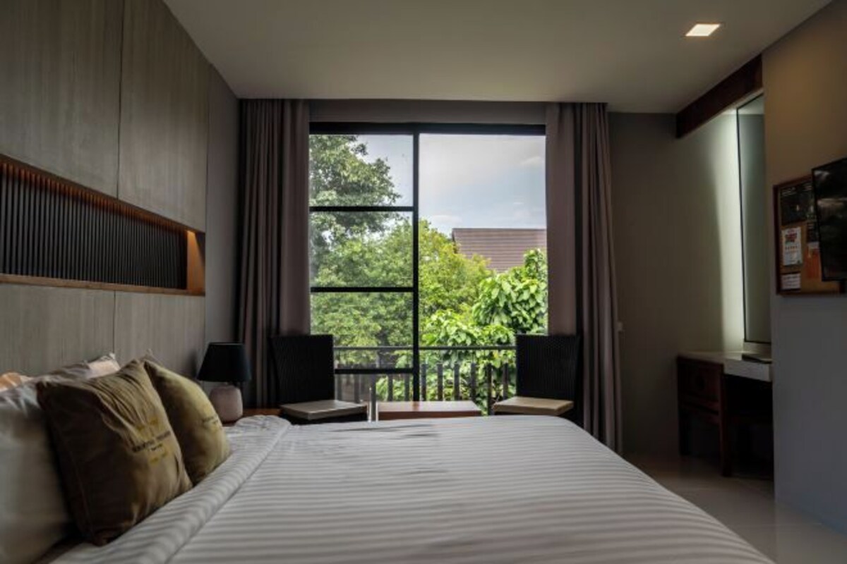 A hotel room with a large bed, a desk, and a view through a window.