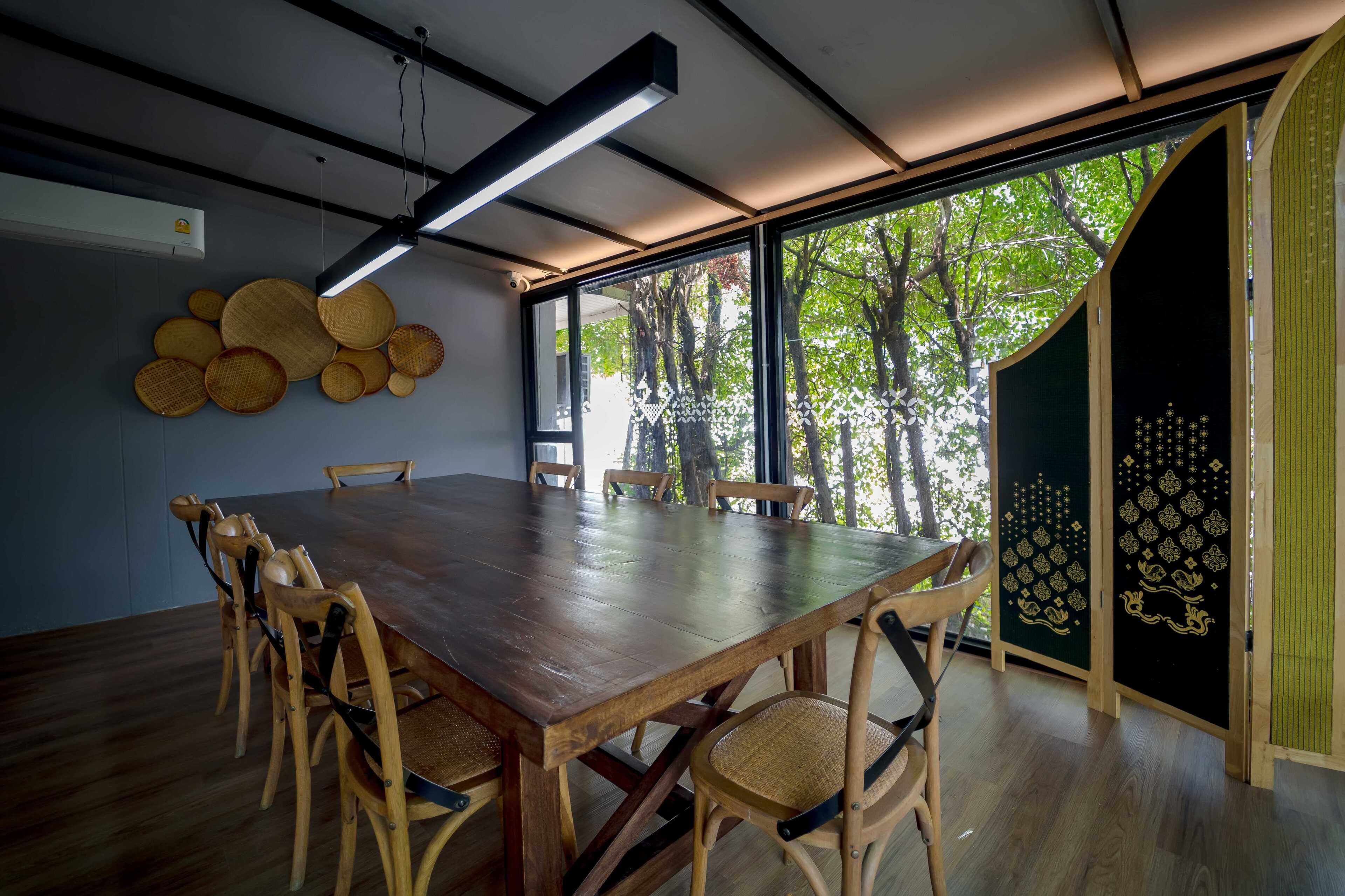 A conference room with a large wooden table and chairs, a ceiling light, and a view of trees through large windows.