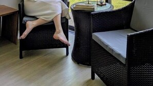 Una habitación con un ventanal grande, una silla de mimbre, una mesita con un globo terráqueo y un libro, y una persona sentada junto a la ventana.