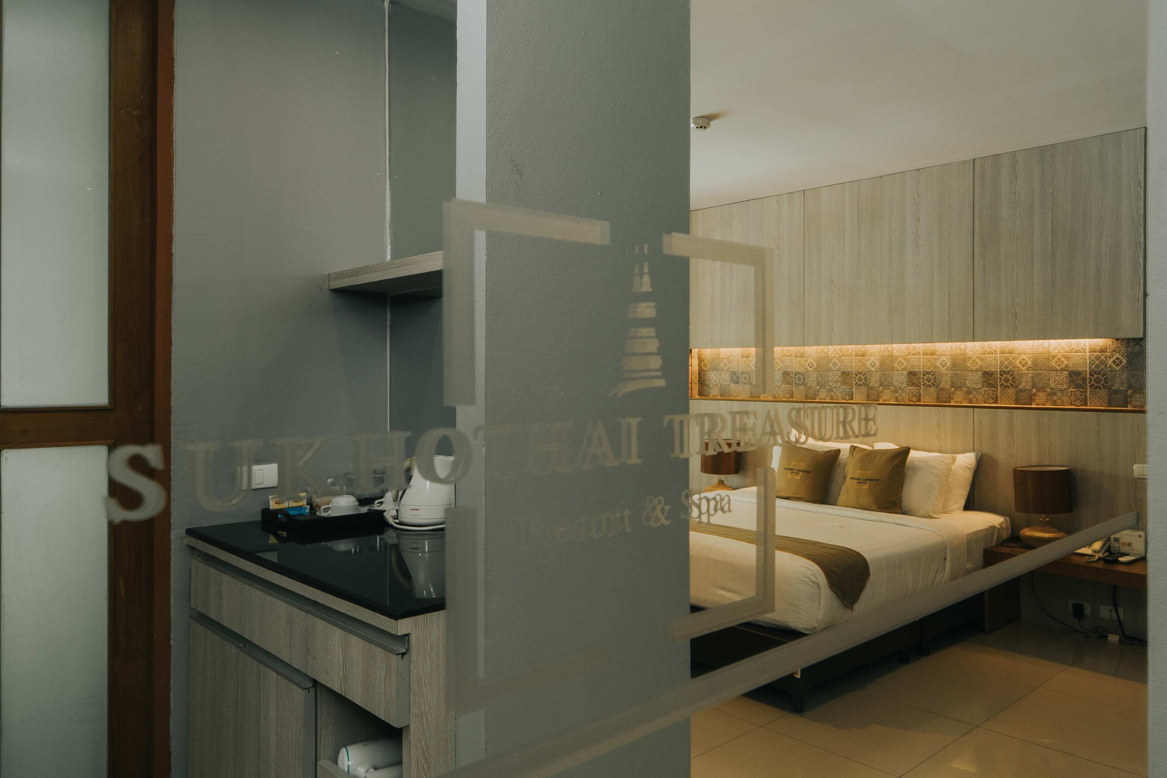 A modern hotel room with a bed, bedside table, and a small kitchenette.