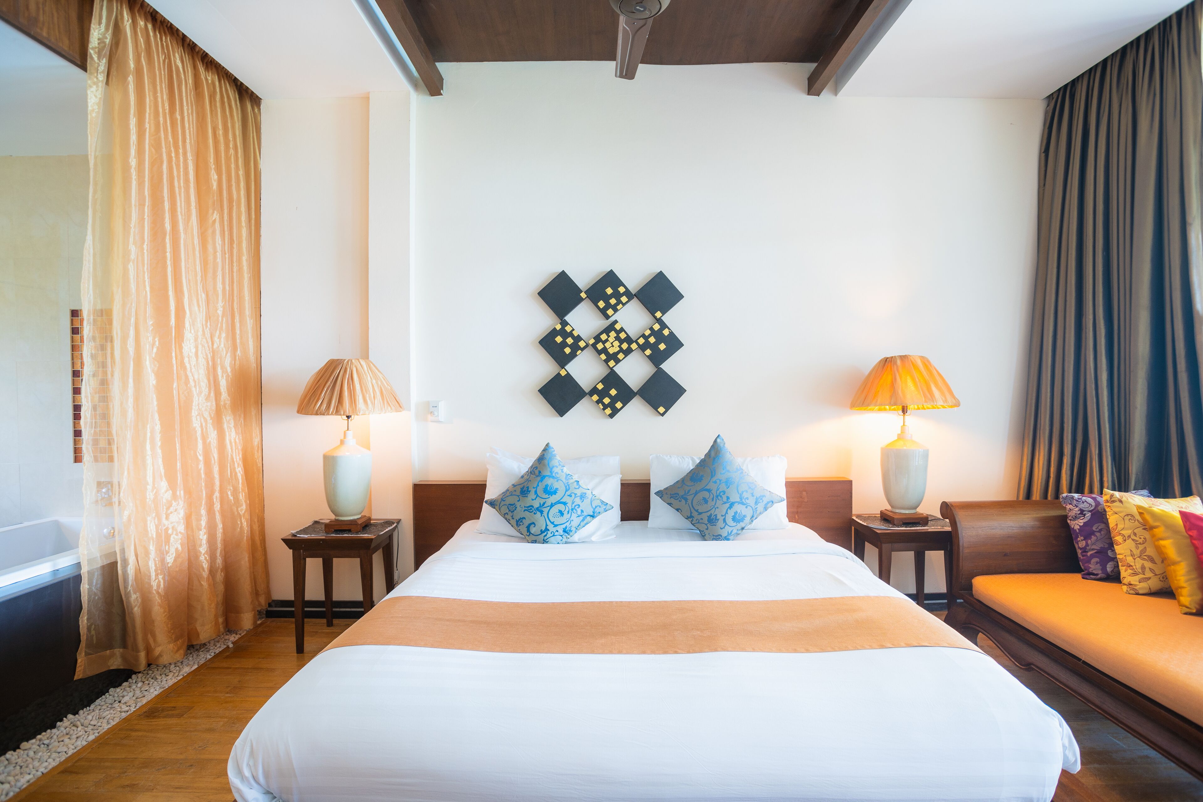 A hotel room with a large bed, two bedside tables with lamps, a headboard with decorative pillows, and a wall art piece.
