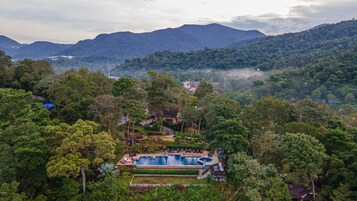 Un resort con piscina rodeada de abundante vegetación y montañas al fondo.