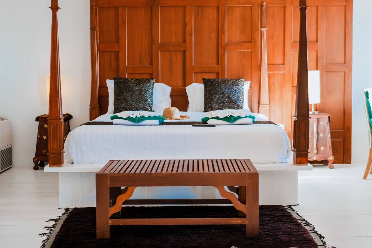 A bedroom with a four-poster bed, a wooden bench, and a dark rug.