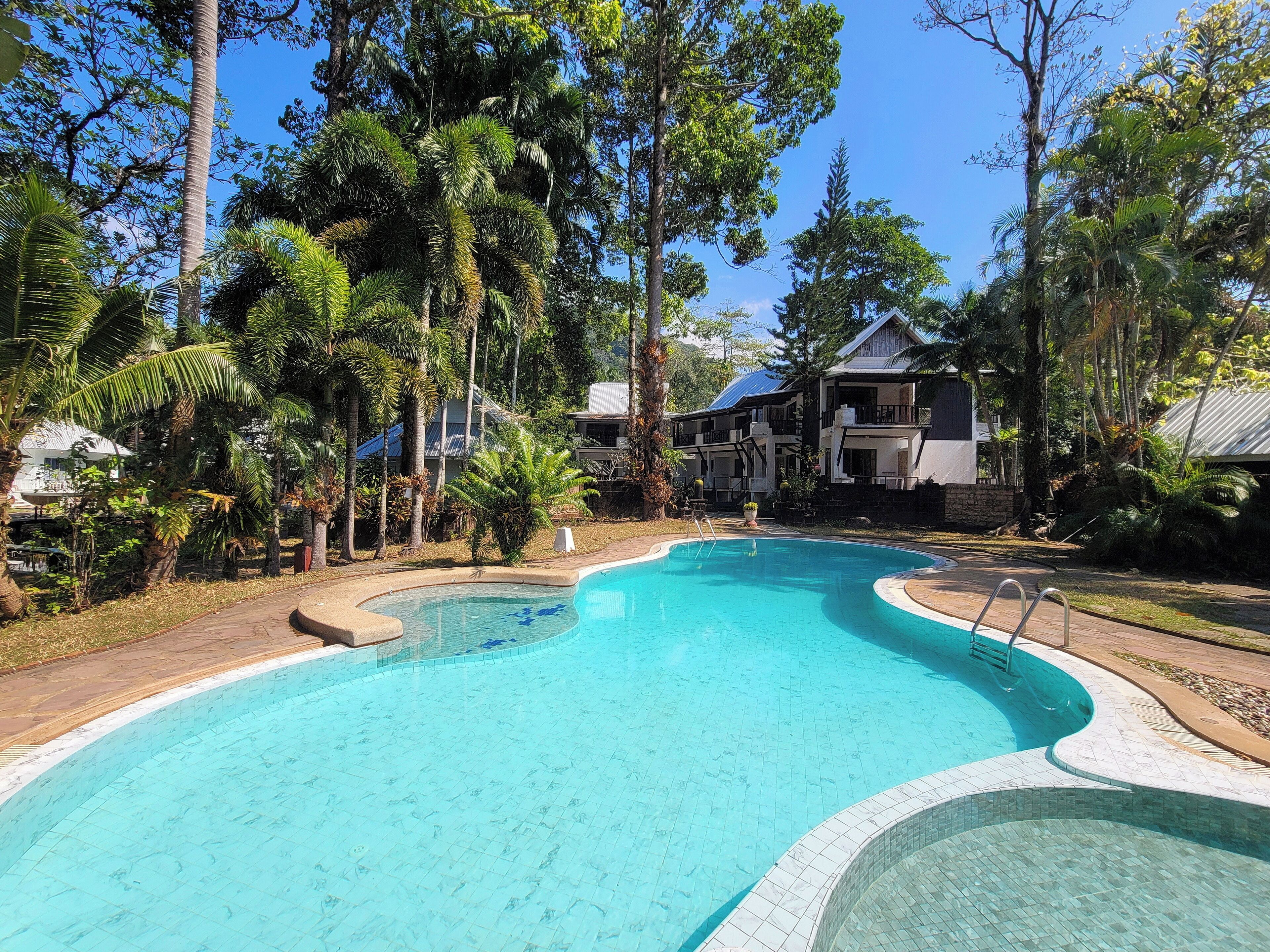 A swimming pool surrounded by lush greenery and a two-story building with a balcony.