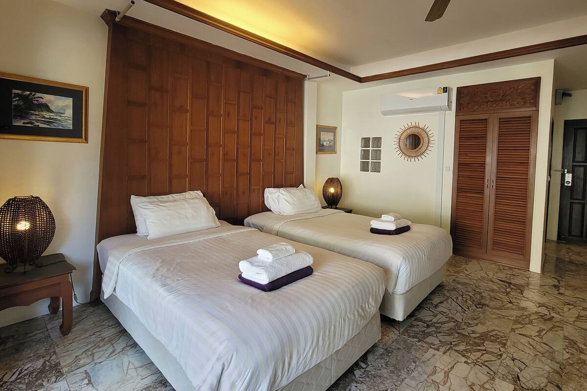 A hotel room with two beds, a wooden headboard, a marble floor, a ceiling fan, and a large mirror.