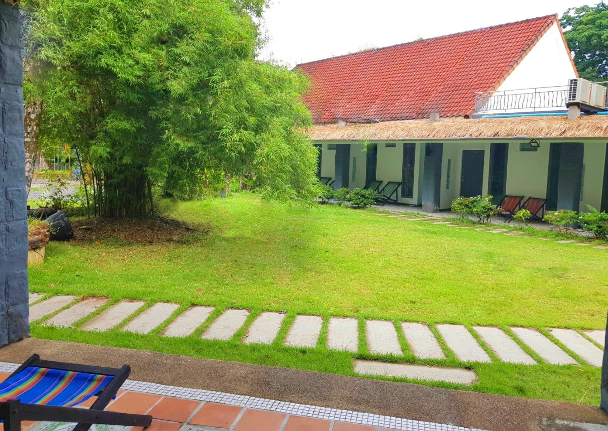 A courtyard with a lawn, a red-tiled roof building, and a seating area with chairs.
